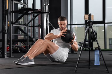 Man with ball streaming online training on phone at gym. Fitness coach