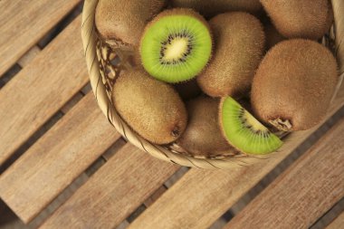 Wicker basket with whole and cut kiwis on wooden table, top view. Space for text