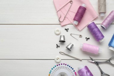 Flat lay composition with thimbles and different sewing tools on white wooden table. Space for text