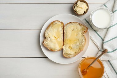 Flat lay composition of sandwiches with butter, honey and milk on white wooden table, space for text