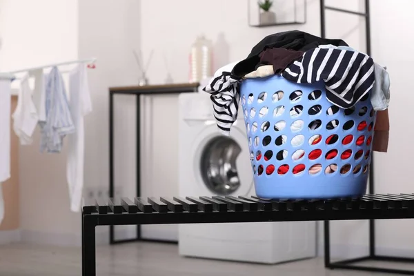 Laundry basket with clothes on black bench in bathroom. Space for text