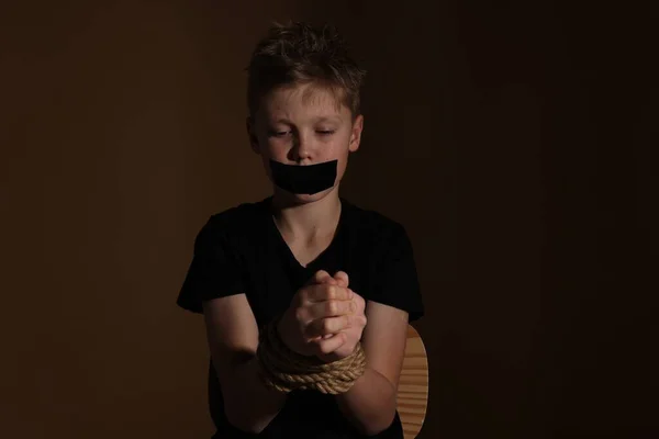 Little boy with taped mouth tied up and taken hostage against dark background