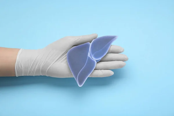 Doctor in glove holding paper liver on light blue background, closeup and top view. Hepatitis treatment