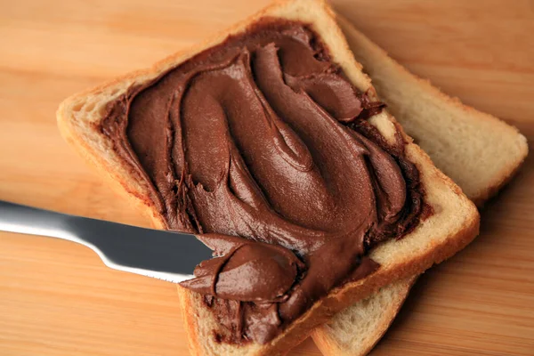Tasty toast with chocolate paste and knife on wooden table, closeup