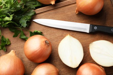 Whole and cut onions with knife and parsley on wooden table, flat lay