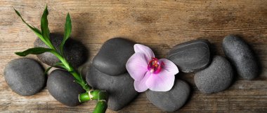 Spa treatment. Flat lay composition with stones, bamboo and orchid flower on wooden table. Banner design