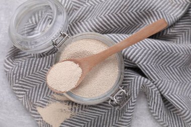 Glass jar and spoon with active dry yeast on light grey table, top view