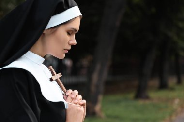 Young nun with Christian cross in park outdoors, space for text