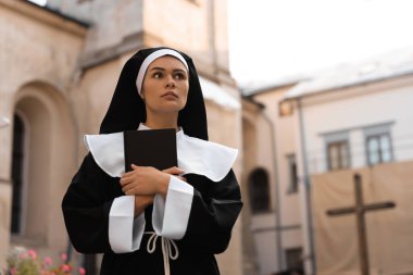 Young nun with Bible near building outdoors, space for text
