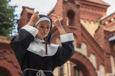 Young nun wearing Christian cross near building outdoors