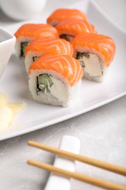Tasty sushi rolls, ginger and chopsticks on grey table, closeup