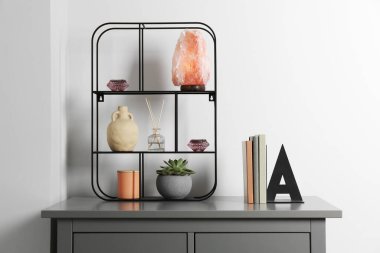 Shelving unit with decorative elements and books on chest of drawers. Interior design