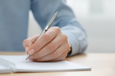 Ahşap masada deftere yazan kadın, yakın plan.