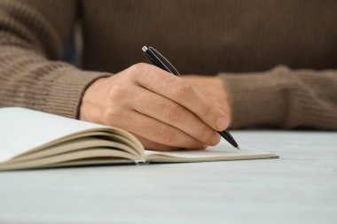 Beyaz masada deftere yazan adam, yakın plan.