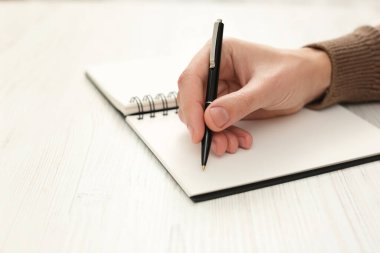 Man writing in notebook at white wooden table, closeup. Space for text