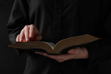 Woman reading holy Bible on black background, closeup