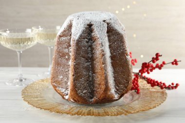 Delicious Pandoro cake decorated with powdered sugar and sparkling wine on white wooden table, closeup. Traditional Italian pastry