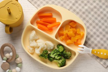 Baby food. Section plate with different vegetables on white wooden table, flat lay