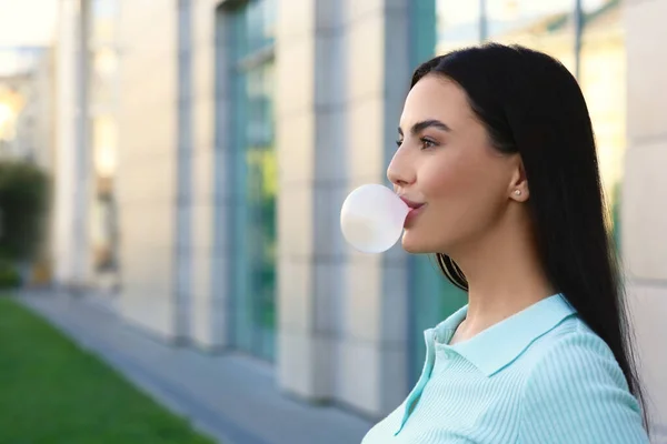 Beautiful woman blowing gum near building outdoors, space for text