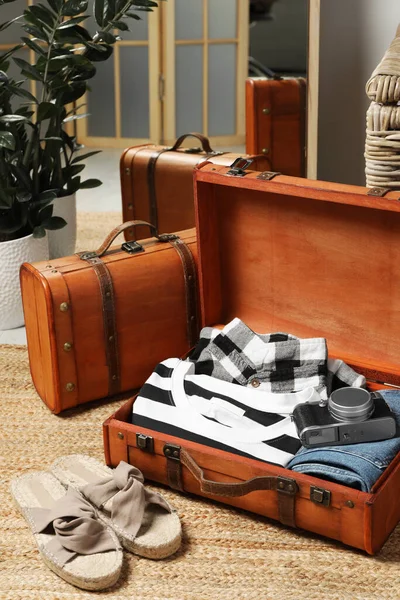 Open suitcase with folded clothes, accessories and shoes on floor in room