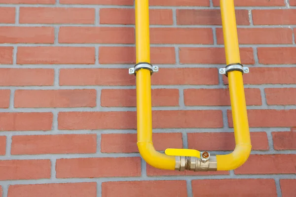 Yellow gas pipe on red brick wall outdoors, space for text