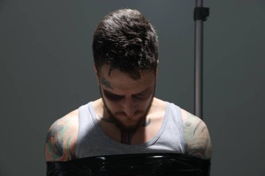 Man with bruise taped up and taken hostage on grey background