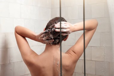 Woman washing hair while taking shower at home, back view