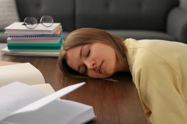 Young tired woman sleeping near books at wooden table indoors