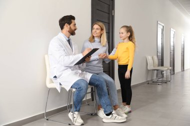 Doctor with clipboard consulting mother and daughter in clinic