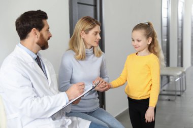 Doctor with clipboard consulting mother and daughter in clinic