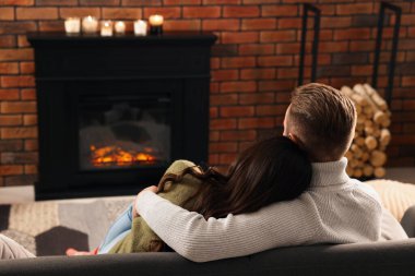 Lovely couple spending time together near fireplace at home, back view