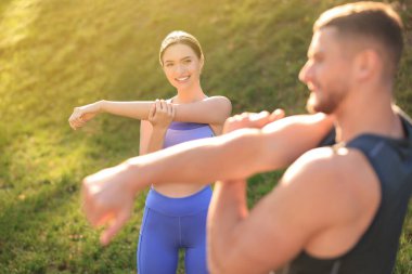 Attractive couple doing sports exercises in park on sunny day. Stretching outdoors