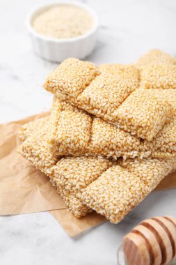 Delicious sweet kozinaki bars, sesame seeds and wooden dipper on white marble table, closeup