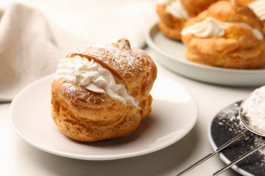 Delicious profiteroles with cream filling and powdered sugar on white table, closeup