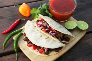 Delicious tacos with meat, vegetables and sauce on wooden table, above view