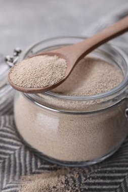 Glass jar and spoon with active dry yeast on light grey table, closeup