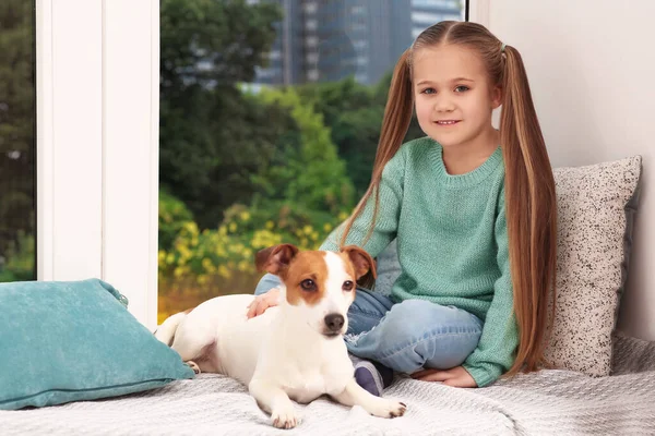 Cute girl with her dog on window sill indoors. Adorable pet
