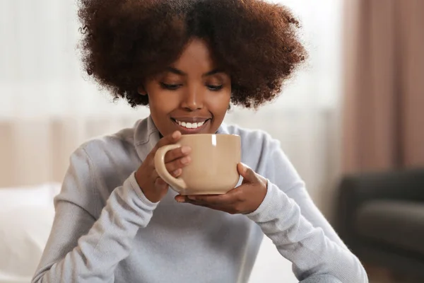 Smiling African American woman with cup of drink at home