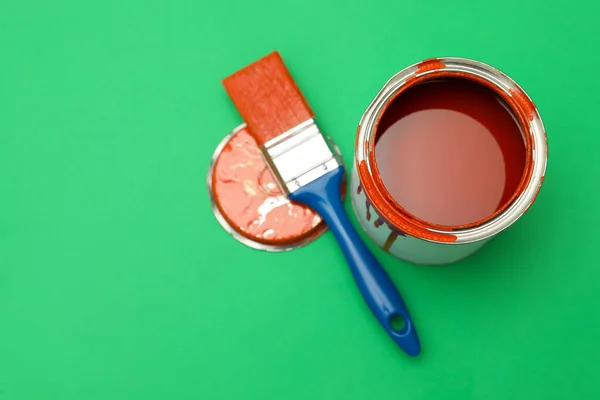 Can of orange paint and brush on green background, flat lay. Space for text