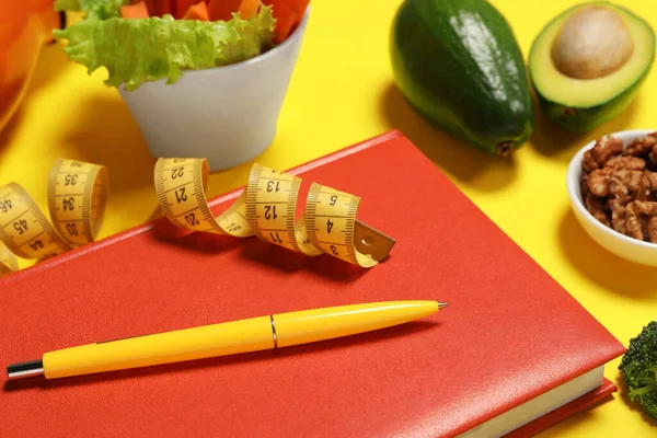 Weight loss concept. Composition with notebook, measuring tape and different products on yellow background, closeup
