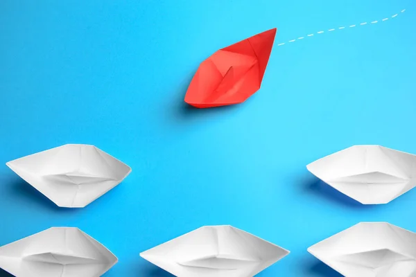Red paper boat floating to others on light blue background. Uniqueness concept