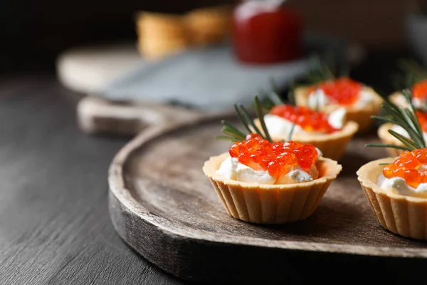 Delicious tartlets with red caviar and cream cheese served on wooden table, closeup. Space for text