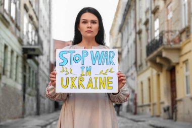 Sad woman holding poster Stop War in Ukraine on city street