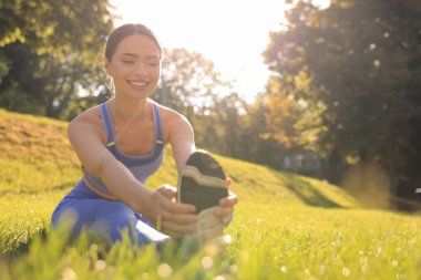 Attractive woman doing exercises on green grass in park, space for text. Stretching outdoors