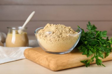 Bowl of aromatic mustard powder and parsley on wooden table