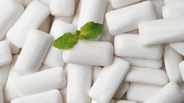 Tasty chewing gums and fresh mint leaves as background, top view