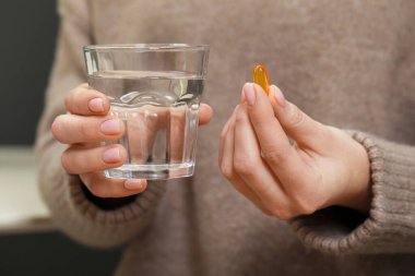 Woman holding glass of water and pill, closeup view