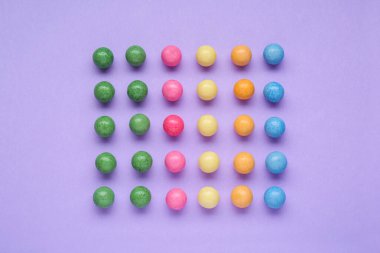 Many bright chewy gumballs on lilac background, flat lay