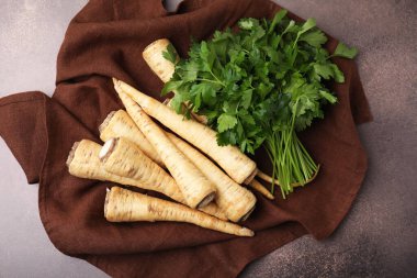 Whole raw parsley roots and bunch of fresh herb on brown table, flat lay