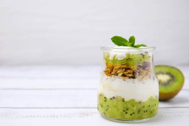 Delicious dessert with kiwi, yogurt and muesli on white wooden table, space for text